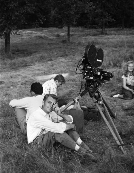 Four members of Madison Youth Council are shown lounging around a movie camera in a woodland setting. They were making a movie, "Make Way for Youth".