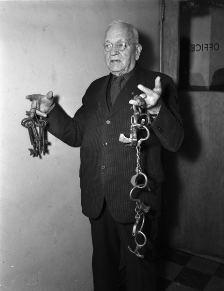 Ernest F. Burmeister, Dane County's "boy" sheriff from 1901-1903 and deputy and turnkey in 1891, is shown holding the keys to the old Dane County jail and the handcuffs he used on unruly prisoners.