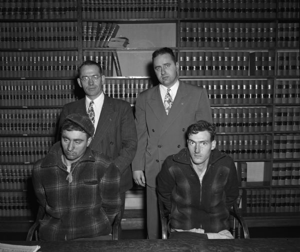 Alleged killers after confessing to the murder of two people. Seated  are Buford Sennett, Richland Center, and Robert Winslow, Owen, standing behind them is Leo P. Lownik, Richland County district attorney, and William J. Coyne, Dane County deputy district attorney.
