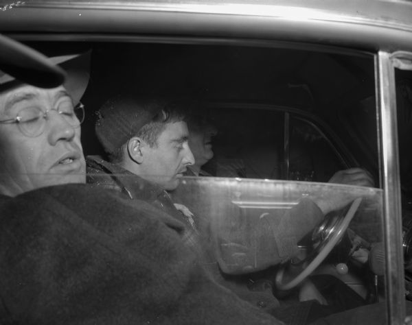 Buford Sennett, confessed murderer, soon after his capture at the Pomputis farm, sitting between a police officer and the driver of the car.