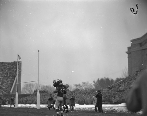 Michigan halfback, Gene Derricette, intercepting a pass intended for Wisconsin's Clarence Self, during their football game at Camp Randall Stadium.