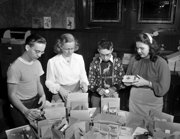 Four members of the Junior Red Cross shown packing boxes for children in the war-torn countries of Europe. From left are Harry Hinze, Central High School; Delores Schlinske, East High School; Don Beran, West High School; and Betty Neesvig, Wisconsin High School.