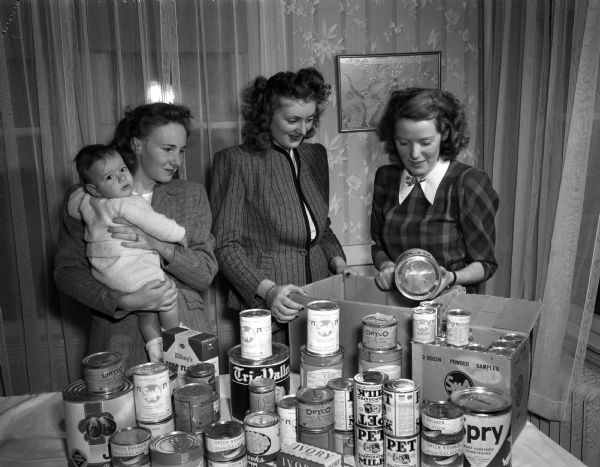 Three French war brides at the French House packing food donated to the Madison committee of Aid to France. Left to right: Mrs. Arthur Indermuchle, holding her baby, Jan; Mrs. Lorne Markham; and Mrs. Joseph Hierscherg.