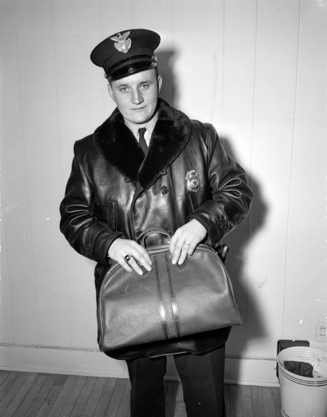 Police officer Raymond P. Kurth holds the leather bag in which the robber, Max M. Feeney, carried the money stolen from the Loraine Hotel.
