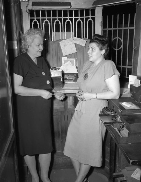 Margaret Foley, left, and Teresa White, right, are shown behind the cashier's window at Hotel Loraine where they were forced at gun point to turn over $154 to the bandit Max M. Feeney, who was captured shortly thereafter by Officer Raymond P. Kurth.