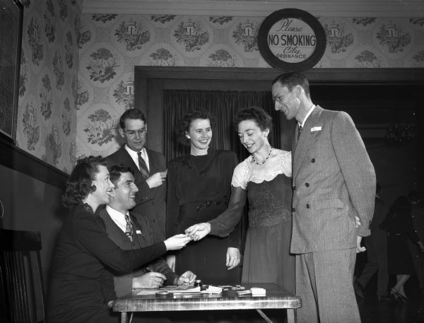 Three couples at the registration desk for the Junior Division of the University League dance. Seated are: John I. and Gardenia Kross; standing left to right: Robert and Winnifred Parent and Earl and Clara E. Bell; Mrs. Bell is president of the Junior Division. The dance was held at the Woman's Building, 240 West Gilman Street.