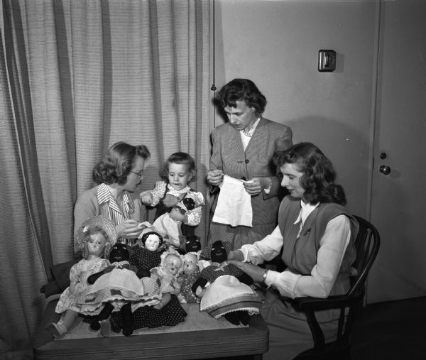 Wisconsin Dames club members sewing doll dresses for dolls to be sold at the Christmas bazaar. Proceeds to be used to purchase Christmas baskets for needy Madison families. Pictured from the left are: Mrs. Arthur (Virginia) English, 22-month old Pamela English, Mrs. Milford (Rosemary) Newman, and Mrs. Gerald Hawkinson.