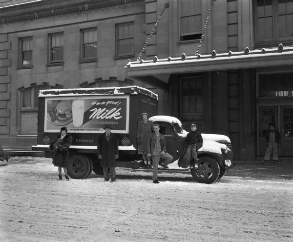Railway Express Agency truck in front of the Chicago and Northwestern Railway station. Seated or standing on the truck are five people (Frost family?). The truck features advertising showing a milk shake and cheeseburger.