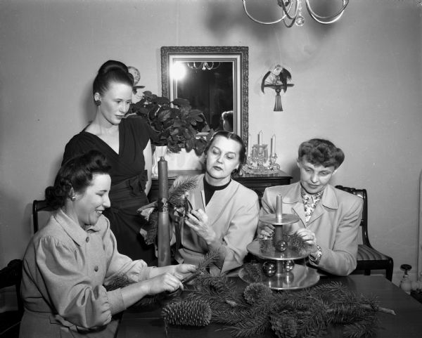 Pictured are committee members of the Navy Officers and Wives Club of Madison who met at the home of Mrs. Robert Huegel to plan the second Christmas dance at the Hotel Loraine. Pictured left to right are: Mrs. Roger Ostrem, standing Mrs. Robert Huegel, Mrs. Winnefred Martin, and Mrs. Raymond L. Kulzick. The seated women are preparing decorations for the dance.