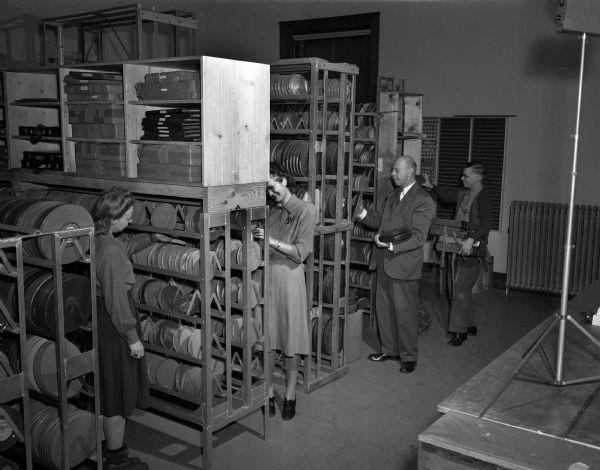 Four people in the stacks of field movies at the University of Wisconsin Bureau of Audio Visual Instruction.  Shown from the left are: Amy Anelerson, Mary Hicks, Joe Berg, and Darwin Carpenter.