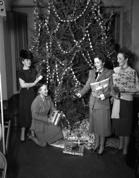 Pictured left to right are: Mrs. Richard Roman, program chairman, Mrs. Norman Wang, president of the East Side Women's club, Mrs. Austin T. Breyer, chairman of the gift project, and Mrs. George Johnson, social chairman of the club. The women are shown with gifts brought for the children at the Morningside Sanitorium, and the Stoughton Orphanage who attend the Club's annual Christmas party at Lowell School.