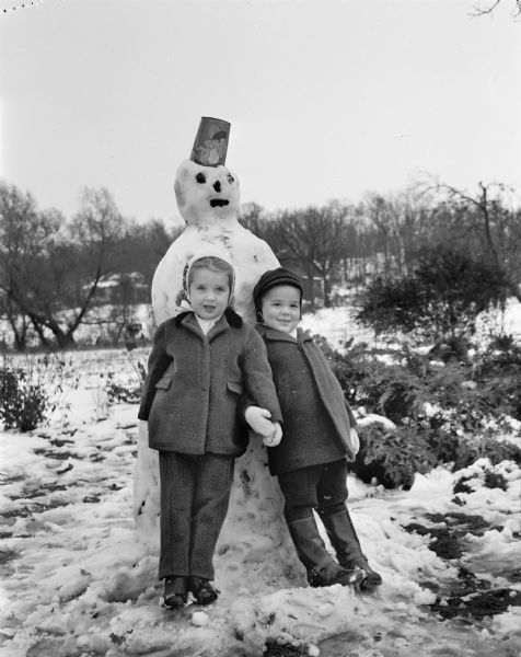 Winter scene with Patty Lou Radder (left) and Ricky Radder posing in front of a snowman they built in their front yard at 3125 University Avenue after a snowfall.