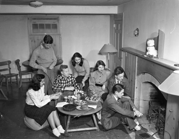 University of Wisconsin-Madison students at a weiner roast in the recreation room of the University of Wisconsin Home Management house at 1430 Linden Drive.  Pictured from left are: Marion Litscher, Sauk City; Lester Swanson, Amery; Bill Wilson, Riverside, Illinois; Laura Taylor, De Pere; Peg Wilson, Dousman; Art Cragoe, Oakfield; and Bud Halker, Fort Atkinson.