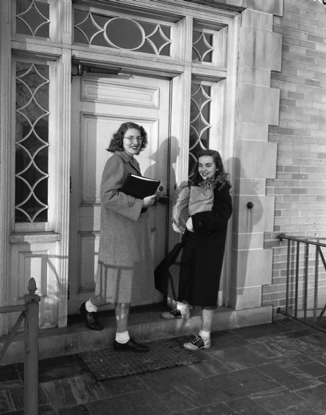 Annette Wellers, Whitewater, hurrying off to class while Mildred Benson, Stoughton, arrives with groceries at the front door of the University of Wisconsin Home Management house at 1430 Linden Drive.  Every senior majoring in home economics was required to live in the house for 2 weeks.