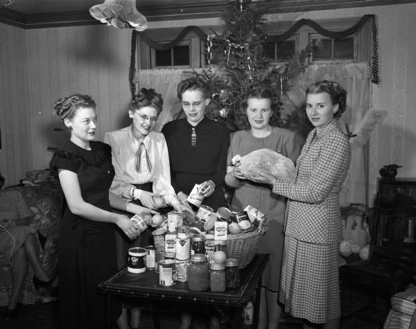 Members of the Junior Chamber of Commerce Auxiliary preparing yule baskets for two families at the home of R.M. (Frances) Larson, 3914 Nakoma Road.  Left to right: Mrs. A.I. (Marcella) Negus, Mrs. Larson, Mrs. Lee (Anna) Miles, Mrs. Lloyd (Helen) Kohl, and Mrs. Marvin V. (Lucille) Bump.