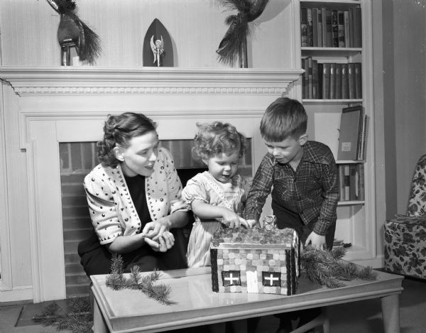 June (Mrs. Robert O.) McLean, and her children Roderick and Gwen, putting the finishing touches on a Gingerbread House.