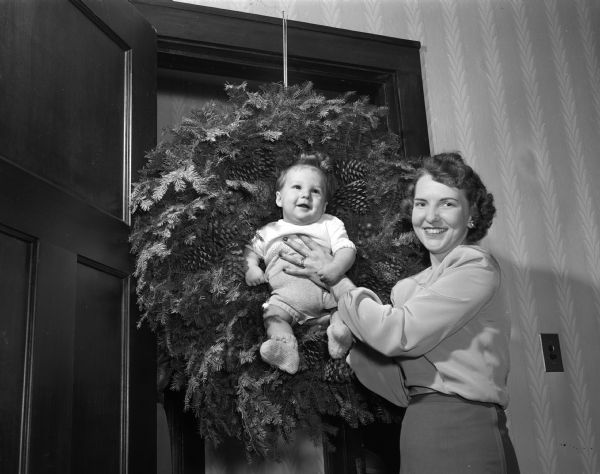 Making an attractive Christmas picture, Janet Woodman holds her baby son, Douglas Shaw, in the center of a huge pine wreath hanging in a doorway.