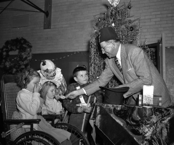Fletcher Mills doing a card trick for three children, with a clown looking on, at the Madison Shriners yule party at the Washington Orthopedic School, 545 West Dayton Street.