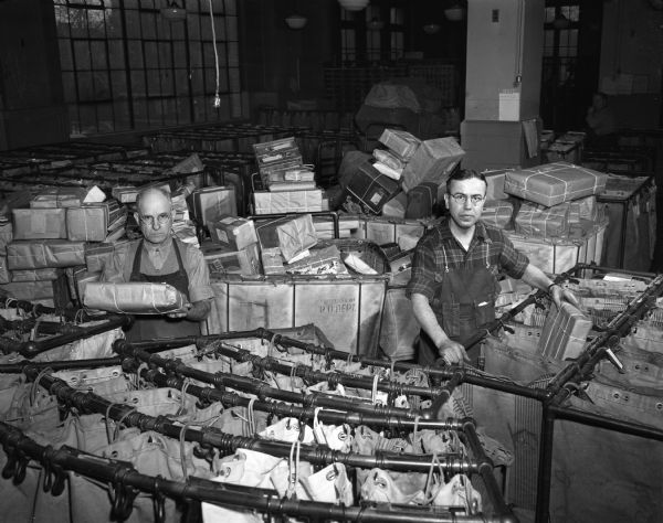 Two postal employees of the Madison post office, 215 Monona Avenue, sorting heaps of packages in carts at Christmas. Pictured from left are clerks Fred Boyd, and Harold Burchette.