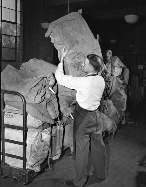 Postal clerk Matt Morrell stacking sacked parcels on a cart at the Madison Post Office, 215 Monona Avenue, to be hauled to the railroad station during the Christmas season.