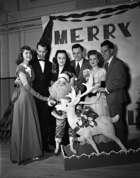 Agnes Dooley, John Fahning, Joe Ann Higgins, Ben Prochaska, Mildred Leach, and Tom Maloney in formal dress standing next to a reindeer and Santa Claus decoration at the Christmas formal party of the Young Adult Club at the Community Center, 16-20 East Doty Street.
