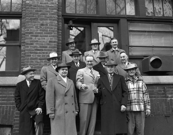 'Roundy' Coughlin receiving a check for $1,085 from eleven contributors for "Roundy's Fun Fund".  The money is to be used for Camp Wawbeek which is located about one mile from Wisconsin Dells.  All eleven men pictured are from the Wisconsin Dells and Lake Delton area, and most are wearing hats and overcoats.