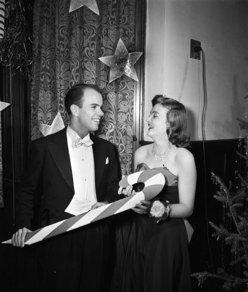 Couple holding a candy cane decoration at the University Club's annual Assembly Ball. Pictured are Donald Easum, son of Prof. and Mrs. Chester V. Easum, 115 North Allen Street, and Rosalie Fred, daughter of University of Wisconsin President and Mrs. Edwin B. Fred, 10 Babcock Drive.