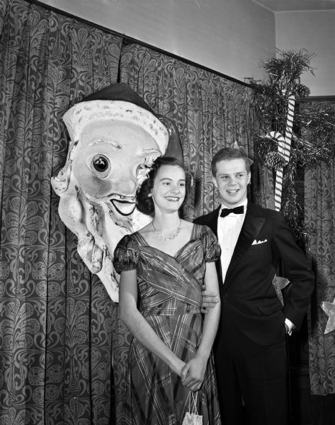 Couple attending the University Club's annual Assembly Ball. Standing in front of a Santa Claus decoration are Janet Easum, daughter of Prof. and Mrs. Chester V. Easum, 115 North Allen Street, and Hartman Axley, son Mr. and Mrs. Ralph E. Axley, 3515 Sunset Drive, Shorewood Hills.