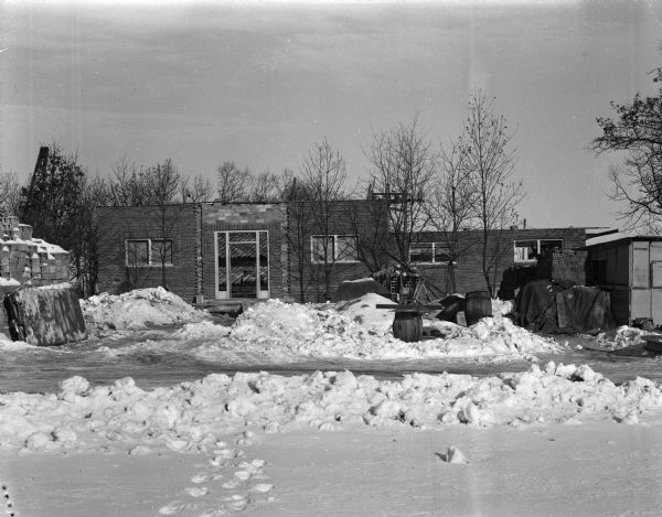 Exterior view of the new building for radio station WIBA under construction. There are piles of snow and building supplies around an entrance.