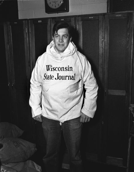 Man standing on front of cabinets modeling a hooded sweatshirt with <i>Wisconsin State Journal</i> printed on the front in large letters.