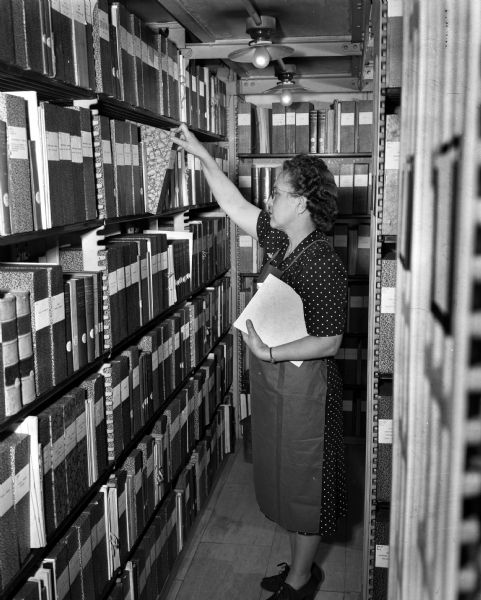 Mrs. Ann Johnson, senior clerk typist, filing clippings in the stacks of the Legislative Reference Bureau stacks.