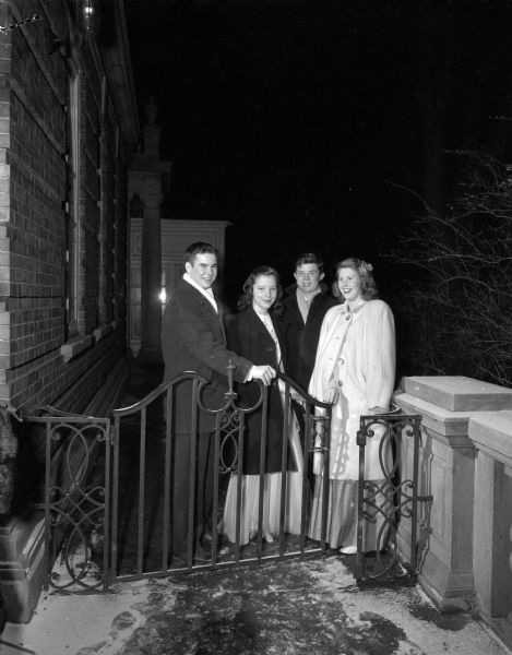 From the left: Michael Dean, Jo Ann Donovan, Cameron Adams, and Mary Weston, at the subscription dance at the Madison club held for the teenage children of club members. They are standing outdoors behind a decorative iron gate.