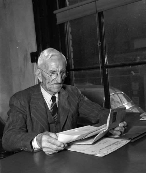 Garrit J. Corscot at his desk near a window, looking at papers in his office, at the Dane County Title Company, 109 South Fairchild Street.
