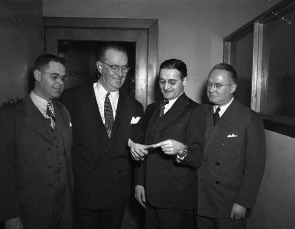 Roundy's Fun Fund committee looking at a check for the benefit of children's activities, including Camp Wawbeek. Pictured are, left to right: Carl H. Waller, director of the Department of Child Study and Service for the Madison Public Schools, "Roundy" Coughlin, Bernard L. Gill, City Purchasing Agent and committee secretary, and Art Trebilcock, president of the Borden Company's Kennedy-Mansfield Division.