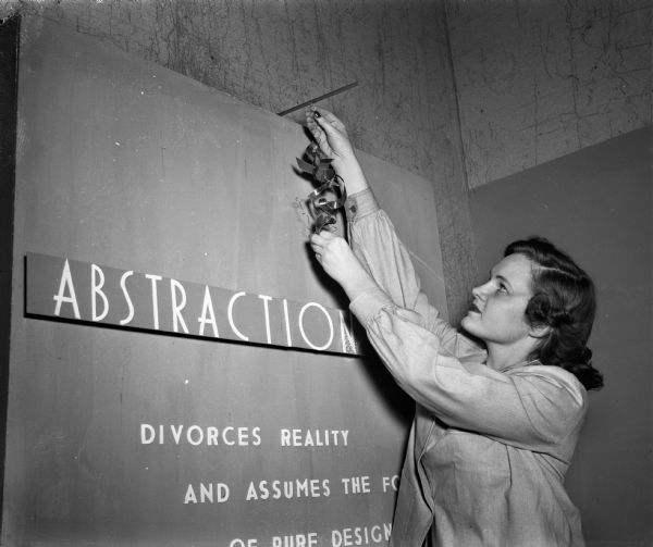 Dorothy Proudfoot, Wilmette, Illinois, shown hanging a sign announcing the University of Wisconsin Memorial Union art exhibit entitled "Abstraction in Art".