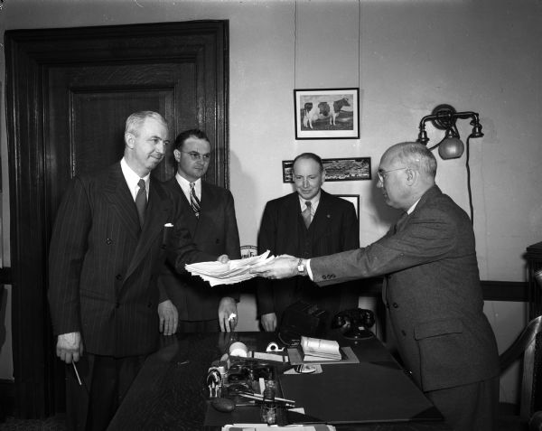 Four staff members of the Marketing division of the Wisconsin Department of Agriculture standing around a desk with a stack of papers.
