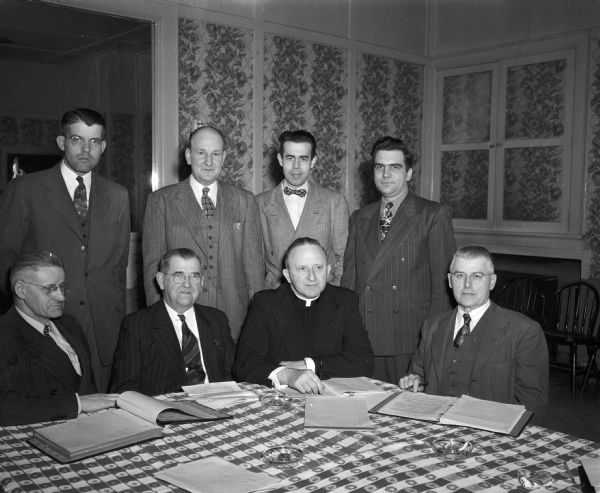 Group portrait of the executive committee of the Holy Name Union for the Catholic diocese of Madison meeting to plan the activities for 1948. Left to right, seated: Bert Walz, vice-president; Dr. J.A. Mudroch, Columbus, president; Rev. Francis X. Gray, Baraboo, spiritual director; George Beyer, secetary.  Left to right, standing: Maurice Leahy, treasurer; Atty. Edward J. Owens, chairman of the lecture bureau; Ken Niglis, chairman of publicity; and Vice F. Deppisch, chairman of retreats and Catholic interests.