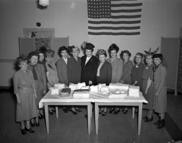 Thirteen members of the American Cancer Society, Cancer Dressing Project, gathered around two tables in front of the American Flag.