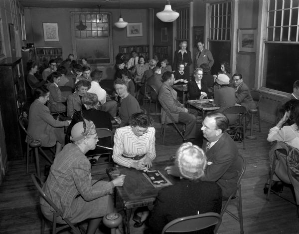 Pictured are a group of Madisonians seated at tables in a large room playing cards at the Madison Community Center, West Doty Street.  The center celebrated its 2nd anniversary in 1948.
