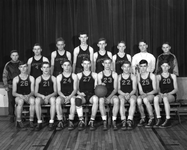 Group portrait of the undefeated Poynette basketball team and their coach, Norbert Brunner. The team won sixteen straight games. They are wearing uniforms and high top tennis shoes.