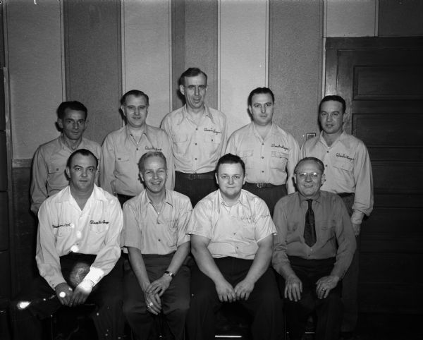 Group portrait of Bank of Madison bowling team, winners of the 1947 Madison bowling championship. Standing left to right: Sam Parisi, Auby Ehrman, Frank Gottsacker, Louis Fiore, and Joe Fedele, captain. Seated left to right: Charles "Chuck" Carey, Eddie Toellner, Ray Erdman, and Glen Vitense. Most of the men are wearing shirts embroidered with the words, "Classic League."