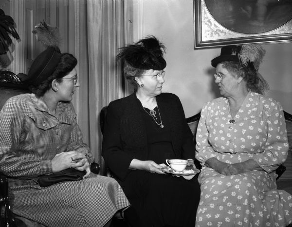 Mrs. Raymond Sayre, Ackworth, Iowa, president of the Associated Country Women of the World, chatting with Miss Eva Belle (left), and Mrs. Walter Pierce, Baraboo, at a tea at the executive residence as part of the University of Wisconsin Farm and Home Week activities. All three women are wearing feathers in their hats.