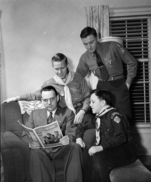 Harlan C. Nicholls, president of the Four Lakes Council of Boy Scouts, and his three sons, all of whom are involved in scouting. Pictured in front at the right is Tony, Cub Scout, standing at right is Herbert, Eagle Scout, and James, also an Eagle Scout. Seated is Mr. Nicholls looking at <i>Scout Executive</i> magazine.