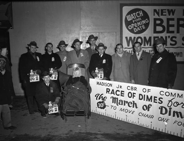 Winning team in the March of Dimes wheelchair race, sponsored by the Madison Junior Chamber of Commerce: Clarence Beebe, kneeling, and in the back row, left to right, Don Eierman, Charles Haynie, Charles Swanson, Bob Zimmerman, Harry P. Stoll, Homer Johnson, Elton Garner, Robert Kohl, and Jack Dewitt. There is a young girl in a wheelchair with a blanket in front of the group.