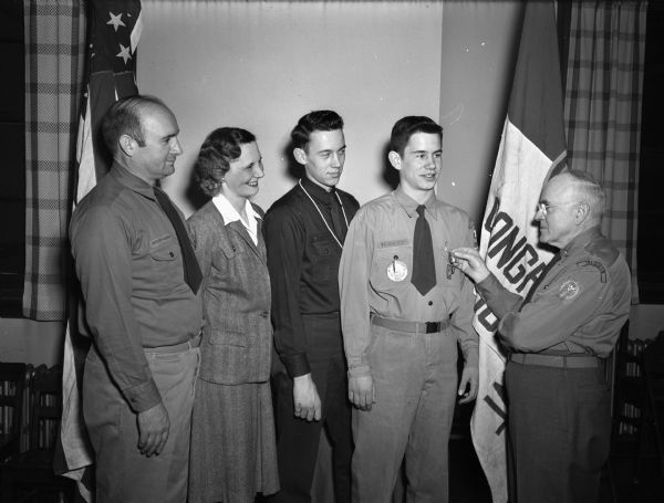 Jerry Hansch receiving his Eagle Scout badge, shown with his parents and one brother, and George Morris, the Four Lakes Council Field Commissioner. Jerry became the third member of his family to receive an Eagle Scout badge.