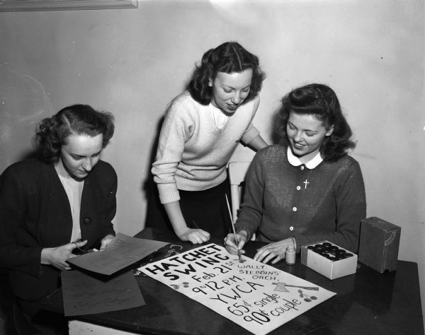 Three young women making posters for the upcoming "Hatchet Swing" dance to be held at the YWCA.  Pictured from the left are: Ann McEvilly, East Hight; Iris Steckling, West High; and Alice Gustavson, West High.