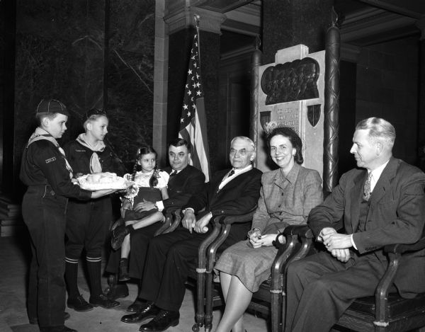 Wisconsin Supreme Court Chief Justice Marvin B. Rosenberry receiving a birthday cake from two Boy Scouts of the Four Lakes council in Lincoln  Day ceremonies in the Wisconsin State Capitol.  Justice Rosenberry, the honorary president of the council, is shown with his son, daughter-in-law, and granddaughter.  The two Cub Scouts are Tom Stafford, left, and Douglas Olson.