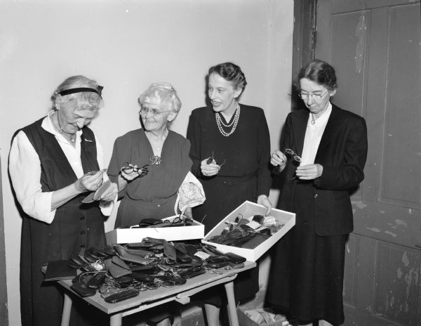 The Religious Society of Friends (Quakers) instigated a collection of eyeglasses to send overseas. Most of the eyeglasses are being sent to Austria at this time. Looking at the collection are: left to right, Flora Mears, Lelia Bascom, Mrs. B.H. (Miriam) Doyon, Helen Johann.