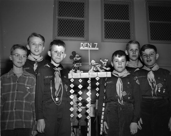 Cub Scout Den 7 of Pack 302, Randall School, at their annual Blue and Gold banquet. They are with a display that depicts Mickey Mouse and probably Pluto, with the boy's names above hooks from which hang tags. Pictured left to right: Donald Johns, Andy McBeath, Bobby Cooper, Tommy Thompson, John Brueckner and Billy Foss.