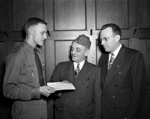Scout Charles Anderson is being presented with a $500 check by Edward Fischer, Sheriff of Dane County, safety director and past commander of the Veterans of Foreign Wars, for rescuing a boy drowning in the Yahara River. At the right is H.C. Nicholls, president of the Council.